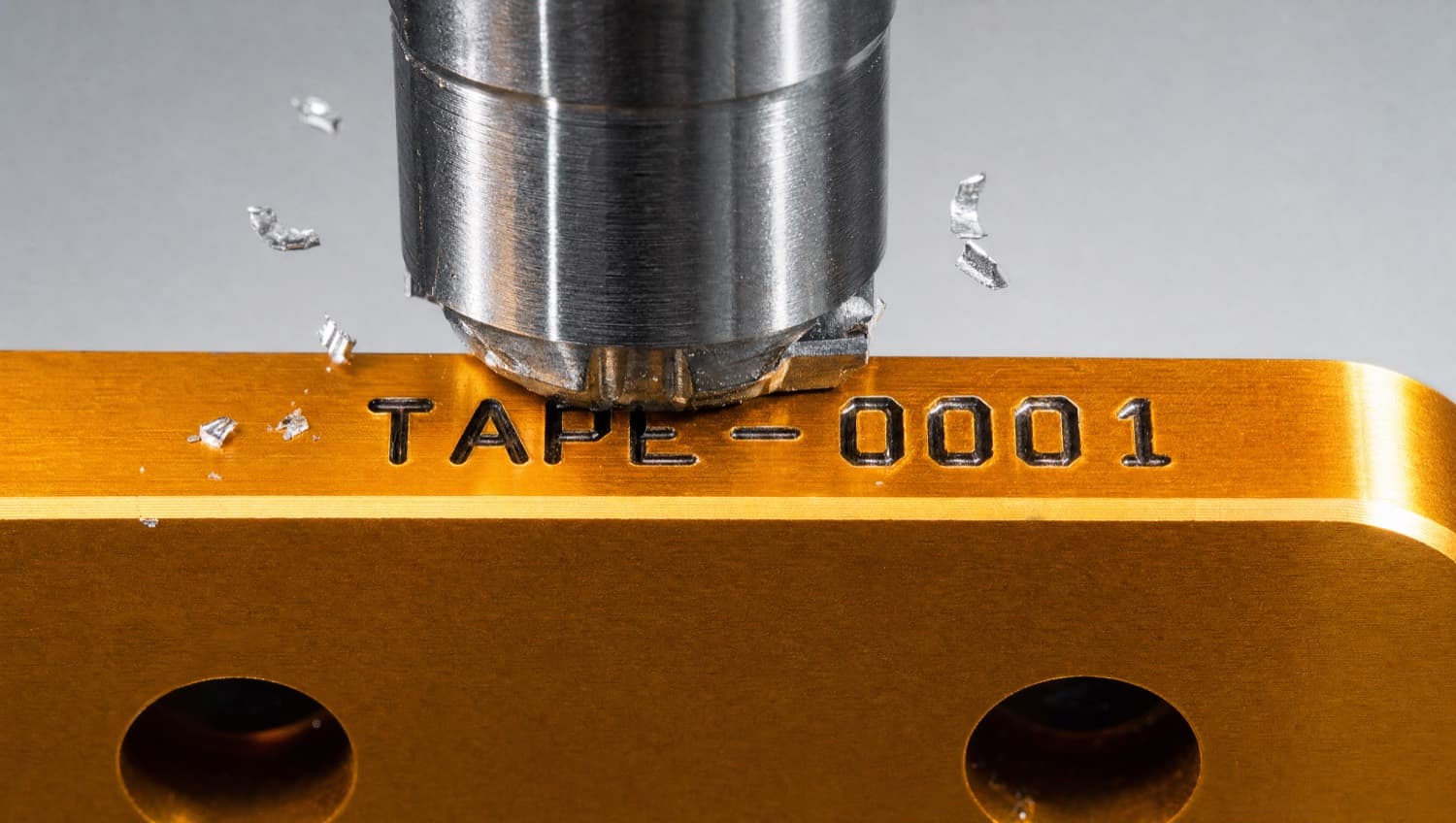 A punch stamping the serial TAPE-0001 into the edge of an amber plate